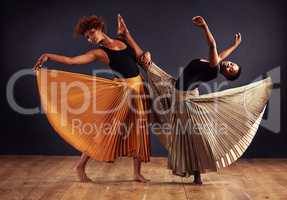 Practice and dedication make perfection. Two contemporary dancers with flowing skirts in front of a dark background.