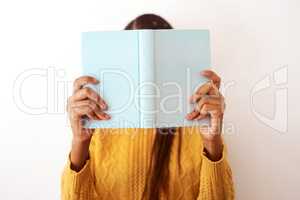 Youll find me behind the books. Studio shot of an unrecognizable woman posing with a book over her face.