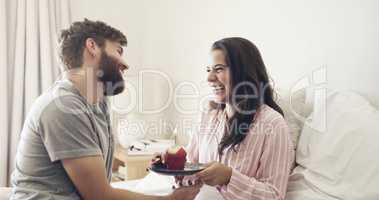 happy birthday to my beautiful wife. Shot of a young man surprising his wife with a cupcake in bed at home.