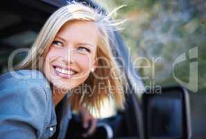 Feeling carefree outdoors. A young woman feeling the breeze in her hair through an open car window.