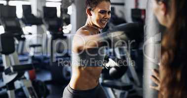 Give it all youve got. Cropped shot of a young female boxer working out on a punching bag with her trainer in the gym.