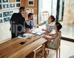 You're just what our team needed. Shot of two businesspeople shaking hands in an office while colleagues look on.