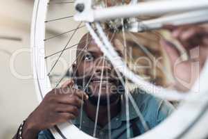 Thats running just the way I like it. Shot of a handsome young man crouching alone in his shop and repairing a bicycle wheel.