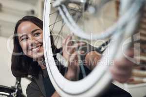 I can see the life lived by this bike. Shot of an attractive young woman standing alone in her shop and repairing a bicycle wheel.