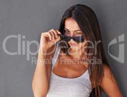 She's such a flirt. Shot of a beautiful young woman peering over her sunglasses and winking.