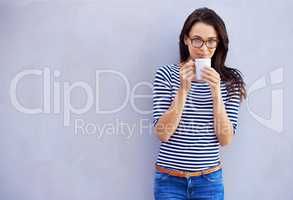 Now that's a fine brew. Portrait of a an attractive woman holding a coffee cup against a gray background.