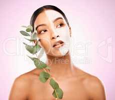Have a pamper day the organic way. Studio shot of an attractive young woman holding a plant and having a facial against a pink background.