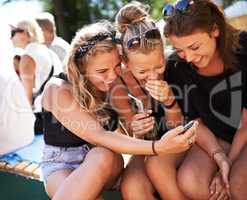 Girls getting in on the gossip. A group of three young girls huddled together and laughing while looking at a cell phone.