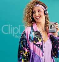 Nothing makes me feel as good as 80s music. Studio shot of a young woman holding a cassette player while dressed in 80s clothing.