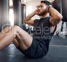 Put all your focus into it. Shot of a sporty young man doing sit up exercises in a gym.