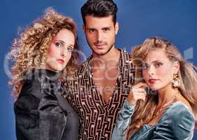 Looking smoking hot in their 80s outfits. Shot of three young people posing together in 80s clothing against a blue background.