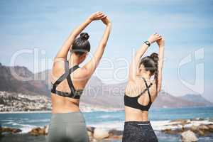 Warming up with a view. Rearview shot of two unrecognizable athletic young women warming up before a wrokout on the beach.