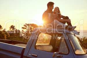 Hilltop romance at sunset. Shot of an affectionate young couple on a roadtrip.