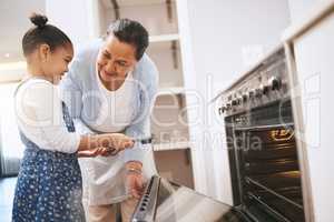 Dont get too close. Shot of a mature woman helping her grandchild safely open the oven at home.