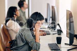 I need to drown out the pressure and stress. Shot of a young call centre agent looking stressed out while working on a computer in an office.