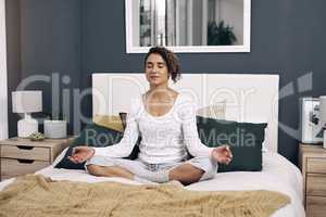 A gesture as strong as faith. Shot of an attractive young woman meditating on her bed at home.