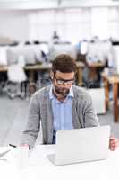 Focused on the finer details. Shot of a handsome young businessman using a laptop in a casual working environment.