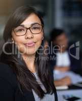 She's an asset to the company. Portrait of a smiling young businesswoman in an office with colleagues in the background.