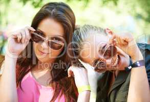 Fun and fashionable. Two young women glancing over the rim of their sunglasses.