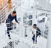 Busy in the corridors of success. Shot of a young professional standing on a stairs with colleagues rushing around him.