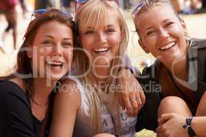 Hanging out with the girls. Portrait of three smiling friends sitting arm in arm and at a festival.