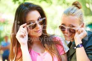 Fun and fashionable. Two young women glancing over the rim of their sunglasses.