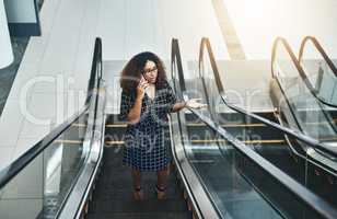 Making business plans on the move. High angle shot of an attractive young businesswoman taking a phonecall while going up an escalator in a modern office.