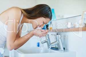 Regular cleansing for skin worth smiling about. Shot of young woman washing her face over the bathroom sink at home.