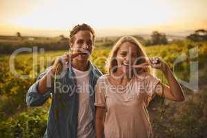 Just testing the produce. Shot of a young couple each holding up a carrot and taking a bite with their crops in the background.