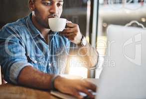 Coffee keeps him focused. Shot of a handsome young man drinking coffee while working working in a cafe.