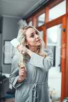 Going through her haircare routine. Shot of a young woman brushing her hair at home.