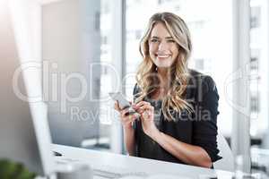 Productivity driven by technology. Shot of a young businesswoman using a mobile phone at her desk in a modern office.