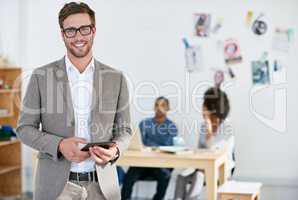 Portrait of a handsome young businessman using a digital tablet with his colleagues in the background. The commercial designs displayed in this image represent a simulation of a real product and have been changed or altered enough by our team of retouchin