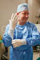 Bringing years of experience and positivity to the ER. Shot of a surgeon putting on surgical gloves in preparation for a surgery.