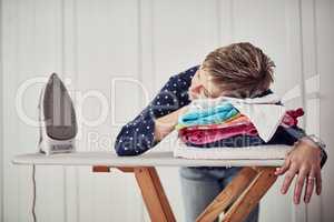 Housework is hectic. Shot of a woman with her head down on a pile of clothes on an ironing board.