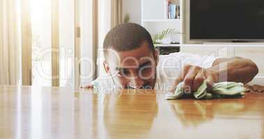 I have to pay attention to detail. Shot of a focused young man cleaning the surface of a table with cleaning equipment at home during the day.