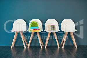 Resources for learning. Studio shot of a row of chairs with books and other learning material on them against a blue background.