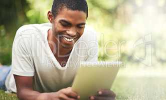 He found a hotspot for happiness. Shot of a young man lying on the grass and using a digital tablet.