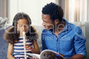 Fathers are often the first teachers in their childrens lives. Shot of a young father teaching his daughter how to play the recorder at home.