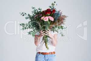 Flowers for someone you love. Studio shot of an unrecognizable woman covering her face with flowers against a grey background.