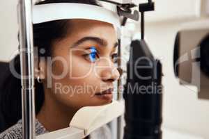 Keep as still as possible. Shot of a young woman getting her eyes examined with a slit lamp.