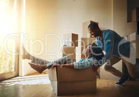 Go faster. Shot of a cheerful young man pushing his girlfriend around in a cardboard box at home during moving day.