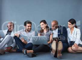 With comfort of the floor, we work together and soar. Studio shot of a group of corporate businesspeople using different devices against a gray background.