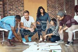 Difficult becomes ease when you have a great team. Shot of a team of entrepreneurs collaborating sitting on the floor in a modern office.