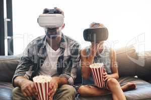 Fun for all ages. Shot of a father and daughter eating popcorn and watching movies with virtual reality headsets at home.