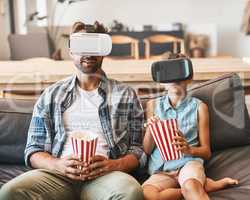 Taking movie night to the next level. Shot of a father and daughter eating popcorn and watching movies with virtual reality headsets at home.