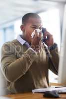 Flu germs have found their way into the office. Shot of a young businessman blowing his nose at his work desk.