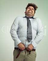 Willing his pants closed. Humorous studio shot of an overweight businessman trying to button his pants.
