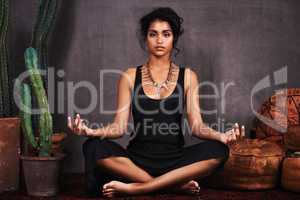 Meditating magic. Studio portrait of a beautiful young woman sitting in the lotus position beside a cactus and cushions.