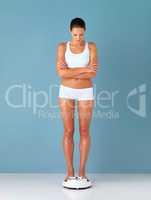 Time to weigh in. Studio shot of a fit young woman weighing herself on a scale against a blue background.
